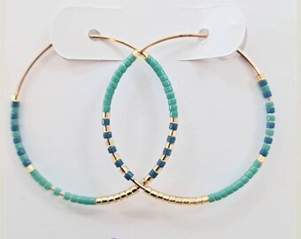 May include: Gold hoop earrings with blue and green beads. The earrings are labeled "Ocean" and "www.richbettejewelry.com".
