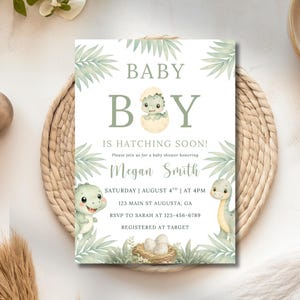 Puede incluir: Una tarjeta de invitación rectangular para baby shower con un dinosaurio verde saliendo de un huevo, rodeado de hojas de palma. El texto dice BABY BOY IS HATCHING SOON! en honor a Megan Smith el sábado 4 de agosto a las 4 PM en 123 Main St.