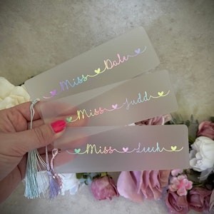 Peut inclure: Trois marque-pages givrés avec des lettres arc-en-ciel irisées. Chaque marque-page porte un nom différent : Miss Balu, Miss Judd et Miss Leech. Chaque nom est entouré de petits cœurs.