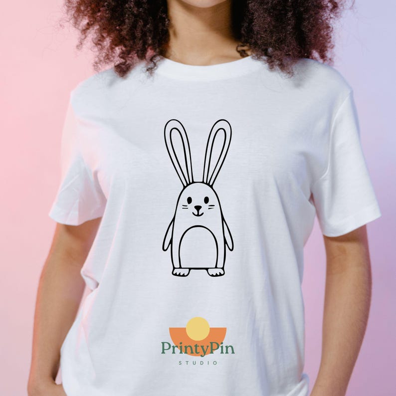 May include: White t-shirt featuring a black and white cartoon bunny design. The bunny has long ears, a small face, and a penguin-like body. The PrintyPin Studio logo is at the bottom.