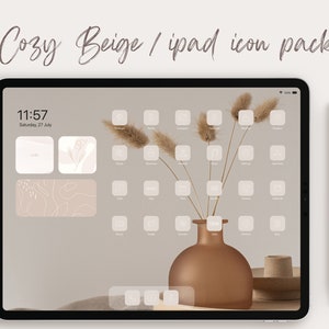 Op de afbeelding: Een beige iPad-scherm met een aangepast pictogrampakket met een minimalistisch ontwerp met witte pictogrammen op een beige achtergrond. Het scherm toont de tijd 11:57 en de datum zaterdag 27 juli. Een witte stylus is rechts van de iPad geplaatst.