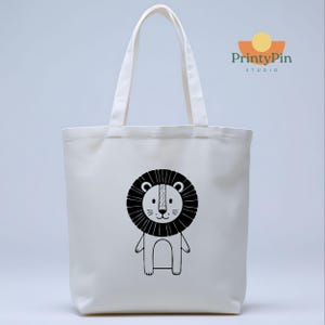 May include: A white canvas tote bag featuring a black and white cartoon lion illustration. The lion has a black mane, a white face, and is standing upright. The bag has two white handles and the PrintyPin Studio logo.