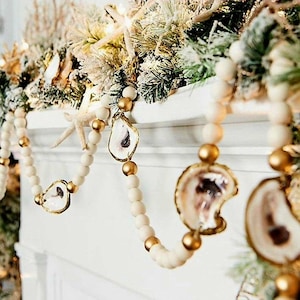 May include: A white and gold beaded garland with oyster shell ornaments. The garland is draped over a white mantelpiece.