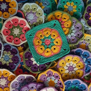 May include: A collection of colourful crocheted granny squares in various colours, including purple, green, yellow, pink, and blue. The squares are arranged in a random pattern on a white crocheted tablecloth.
