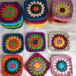 Könnte beinhalten: Neun bunte gehäkelte Quadrate mit einem Blumendesign in der Mitte. Die Quadrate sind aus verschiedenen Garnfarben gefertigt, darunter Lila, Grün, Orange, Gelb, Rosa und Blau.