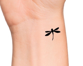 May include: A black silhouette of a dragonfly tattoo on a person's wrist.