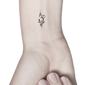 May include: A small black Om symbol tattoo on a person's wrist.