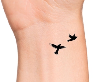 May include: A close-up of a person's wrist with a simple tattoo of two black birds in flight.