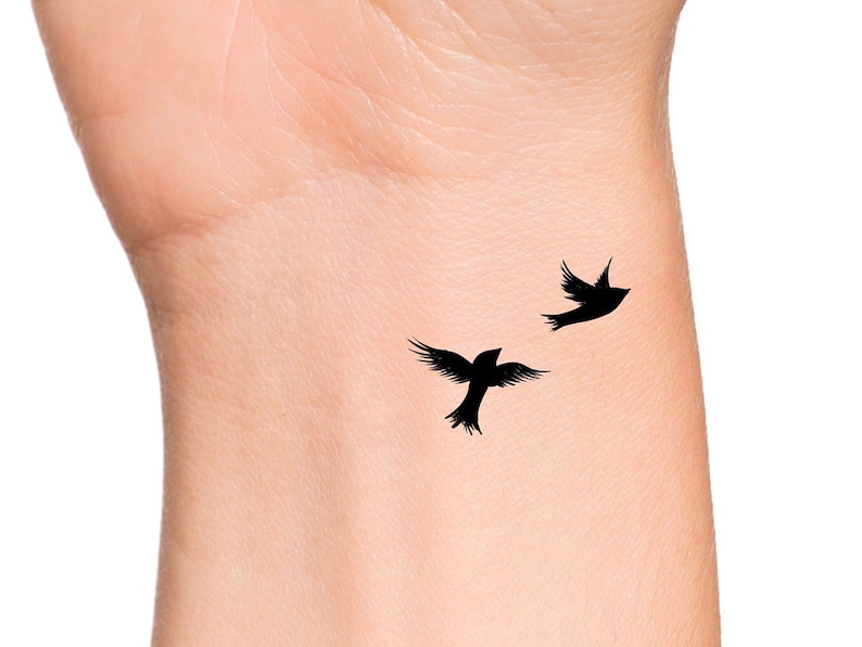 May include: A close-up of a person's wrist with a simple tattoo of two black birds in flight.