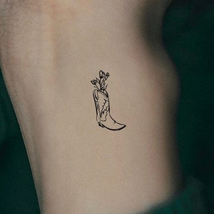 May include: A black line drawing tattoo design of a cowboy boot with flowers growing out of the top.