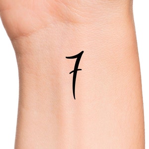 May include: A close-up of a person's wrist with a simple black tattoo of the number "7" written in a cursive font.