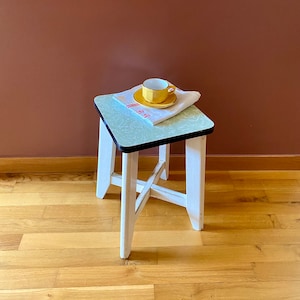 Könnte beinhalten: Ein weißer Hocker mit einer grün-weißen Linoleumplatte. Eine gelbe Teetasse und Untertasse stehen auf einem weißen Papiertuch auf dem Hocker.