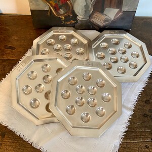 Peut inclure: Quatre plateaux de service octogonaux en argent avec un bord surélevé et 12 indentations pour servir des escargots. Chaque plateau porte le mot "RUE" en relief sur le dessus.