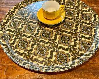 May include: A round, white tray with a green and gold paisley pattern. A yellow saucer and a white teacup are on the tray.