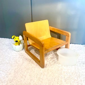 May include: A small wooden chair with a light brown finish. The chair has a simple design with a rectangular frame and a square seat. The chair is sitting on a white fluffy rug.