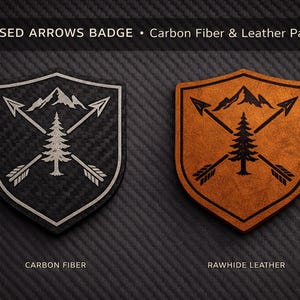 May include: Two shield-shaped patches with a mountain, tree, and crossed arrows design. One is black carbon fiber with a white outline, the other is rawhide leather with a black outline. Text at the top reads "Crossed Arrows Badge".