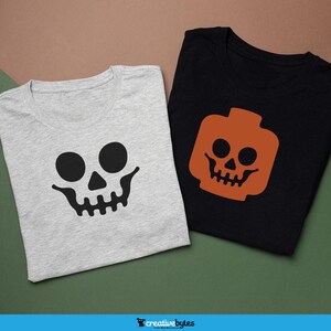Op de afbeelding: Twee T-shirts met een schedelontwerp. Eén T-shirt is grijs met een zwarte schedel, en de andere is zwart met een oranje schedel.
