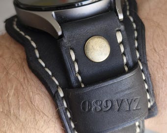 May include: A black leather cuff watch strap featuring white contrast stitching, a metallic brass-colored snap button, and the embossed alphanumeric text 089 VYZ. The strap is attached to a circular watch face with a dark metallic frame.