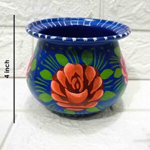 May include: A hand-painted blue ceramic pot with a white rim and floral designs. The pot is 4 inches tall and features red and pink roses with green leaves.