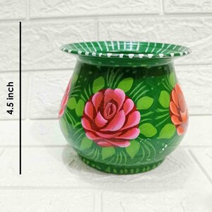May include: A green painted metal pot with a white rim, decorated with pink and red roses and green leaves. The pot is 4.5 inches tall.