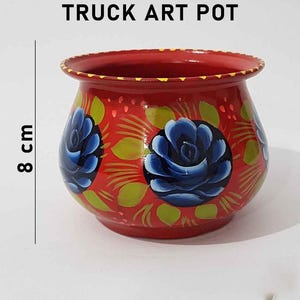 May include: Red truck art pot with blue and green floral designs. The pot is 8 cm tall.