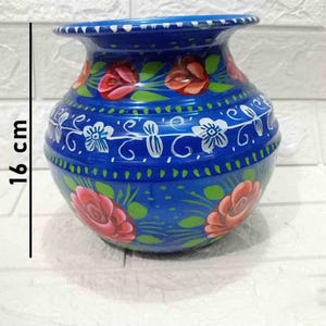 May include: A blue ceramic pot with hand-painted floral designs. The pot is 16 cm tall and features white, green, and red flowers.