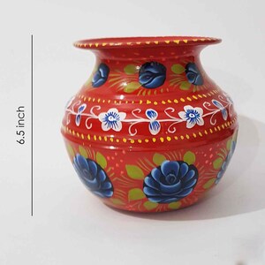 May include: A red, hand-painted metal pot with blue and white floral designs. The pot is 6.5 inches tall.