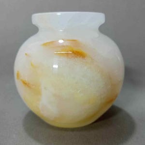 May include: A small, round vase with a swirl pattern of yellow and orange. The vase is made of alabaster.