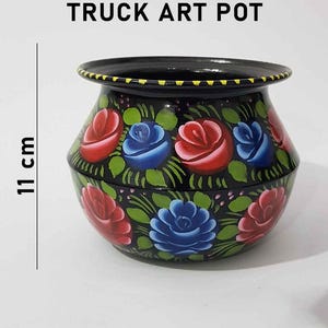 May include: Black metal pot with hand-painted floral design. The pot is decorated with red, blue, and green roses. The pot is 11 cm tall. Truck Art Pot.