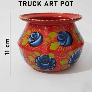 May include: Red truck art pot with blue and green floral designs. The pot is 11 cm tall.
