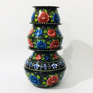 May include: A set of three black, hand-painted decorative pots. Each pot features red and blue roses, green leaves, and white floral details. The pots are stacked, creating a unique decorative display. The pots are a decorative item.
