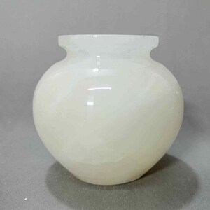 May include: A white alabaster vase with a round body and a slightly flared rim. The vase has a smooth, polished finish and a subtle, swirling pattern.