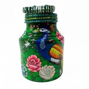 May include: A hand-painted green glass bottle with a peacock design. The bottle is decorated with pink, white, and blue flowers, and the peacock has blue and yellow feathers. The bottle has a green lid with a decorative pattern.