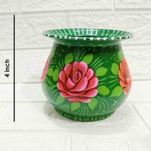 May include: A green hand-painted ceramic pot with a floral design. The pot is decorated with pink and red roses and green leaves. The pot is 10 cm tall.