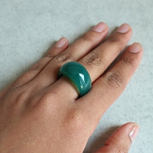May include: A green agate ring with a rounded, smooth surface. The ring is worn on a finger.