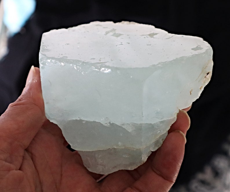 May include: A large, translucent, light blue aquamarine crystal with a rough, natural texture. The crystal is shaped like a block with several layers.