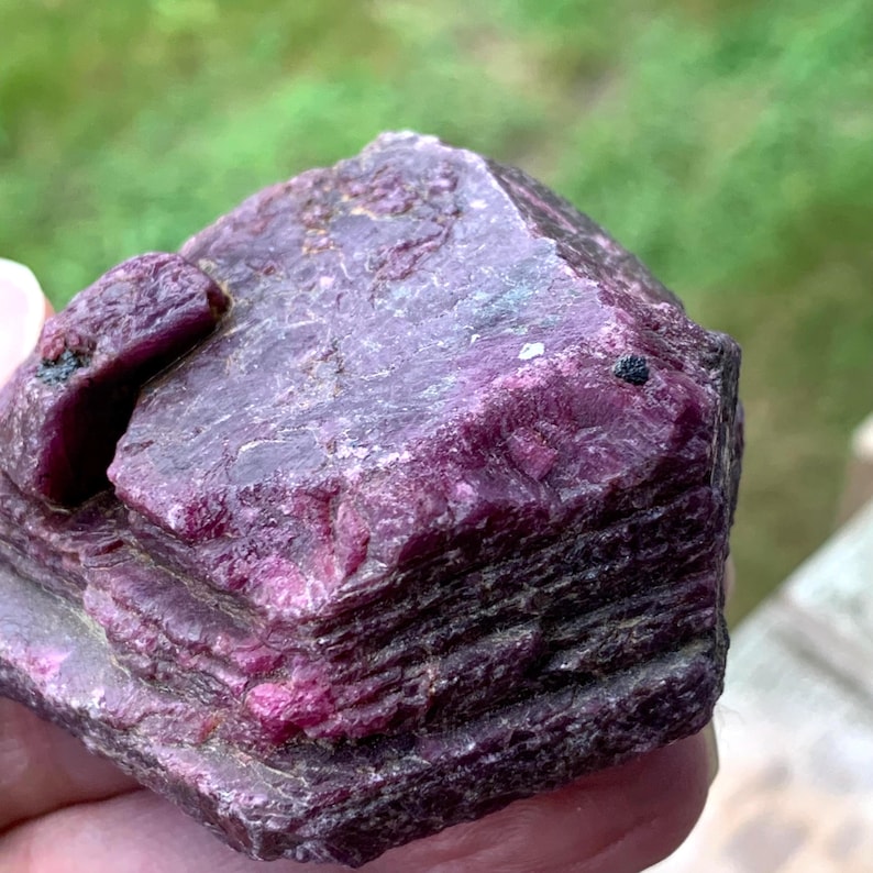 Top-angle rough ruby stone, uneven surface with bright pink flashes and burgundy tones, natural ruby specimen.
