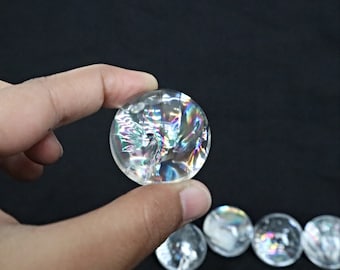 May include: A collection of clear crystal spheres with iridescent rainbow colours. The spheres are smooth and polished, and they are arranged in a row on a black surface.