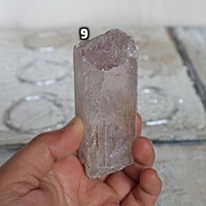May include: A translucent, light pink crystal with a rough, natural texture. The crystal is shaped like a prism and has a slightly cloudy appearance.