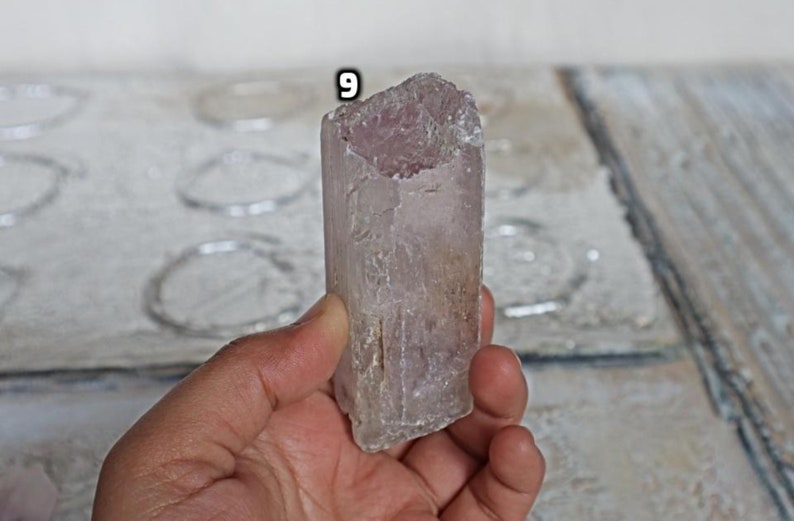 May include: A translucent, light pink crystal with a rough, natural texture. The crystal is shaped like a prism and has a slightly cloudy appearance.