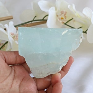 May include: A large, light blue aquamarine crystal with a rough, natural texture. The crystal is translucent and has a slight shimmer.