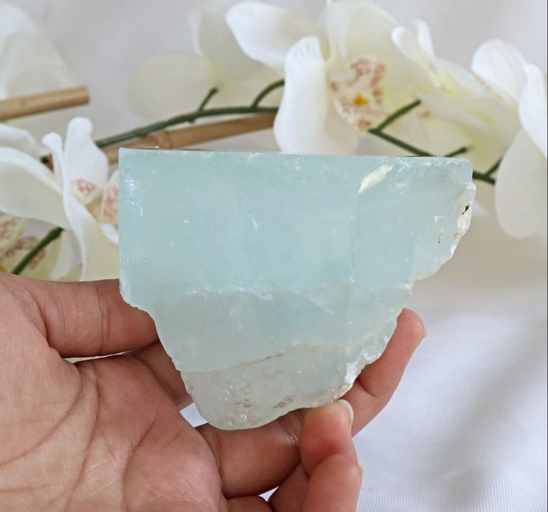 May include: A large, light blue aquamarine crystal with a rough, natural texture. The crystal is translucent and has a slight shimmer.