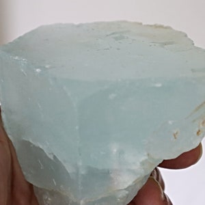 May include: A large, light blue aquamarine crystal with a smooth, polished surface. The crystal has a slightly cloudy appearance and is irregularly shaped.