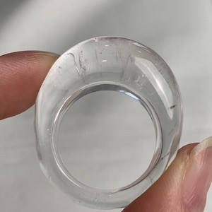 Op de afbeelding: Een heldere, transparante ring met een gladde, ronde band. Het materiaal ziet eruit als glas of acryl en heeft een dikke, massieve constructie met zichtbare interne reflecties en subtiele lichtbrekingen door de gehele cirkelvorm.