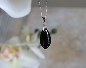 以下が含まれることがあります： 黒いしずく型のペンダントが付いたシルバーのネックレス。ペンダントは滑らかで光沢があり、光を反射します。チェーンは繊細で、ペンダントの上部にある小さなベイルから吊り下げられています。これはジュエリーで、おそらくネックレスです。