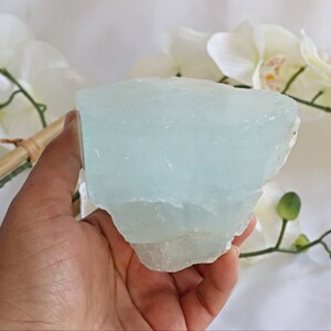 May include: A large, light blue aquamarine crystal with a rough, natural texture. The crystal is translucent and has a slight shimmer.