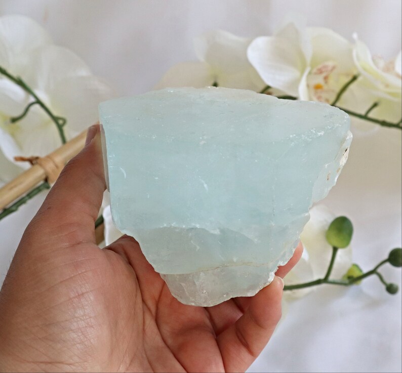 May include: A large, light blue aquamarine crystal with a rough, natural texture. The crystal is translucent and has a slight shimmer.