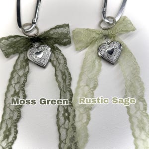 Peut inclure: Deux porte-cl&eacute;s avec des rubans en dentelle et des m&eacute;daillons en forme de c&oelig;ur. L'un a un ruban vert mousse, l'autre un ruban vert sauge. Le texte "Moss Green" et "Rustic Sage" est imprim&eacute; en dessous.
