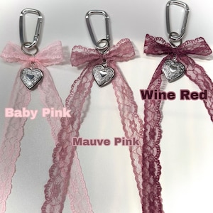 Peut inclure: Trois porte-cl&eacute;s avec des rubans en dentelle rose b&eacute;b&eacute;, rose mauve et rouge vin. Chaque porte-cl&eacute;s comporte un charm en forme de c&oelig;ur argent&eacute; et un mousqueton argent&eacute;. Les textes "Baby Pink", "Mauve Pink" et "Wine Red" sont affich&eacute;s.