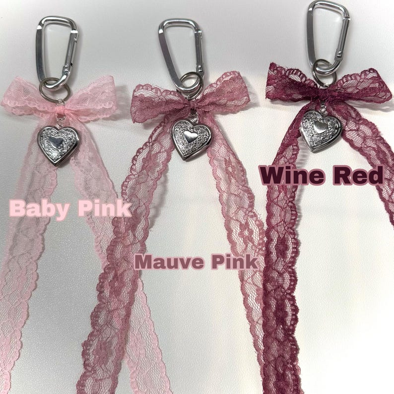 Peut inclure: Trois porte-cl&eacute;s avec des rubans en dentelle rose b&eacute;b&eacute;, rose mauve et rouge vin. Chaque porte-cl&eacute;s comporte un charm en forme de c&oelig;ur argent&eacute; et un mousqueton argent&eacute;. Les textes "Baby Pink", "Mauve Pink" et "Wine Red" sont affich&eacute;s.